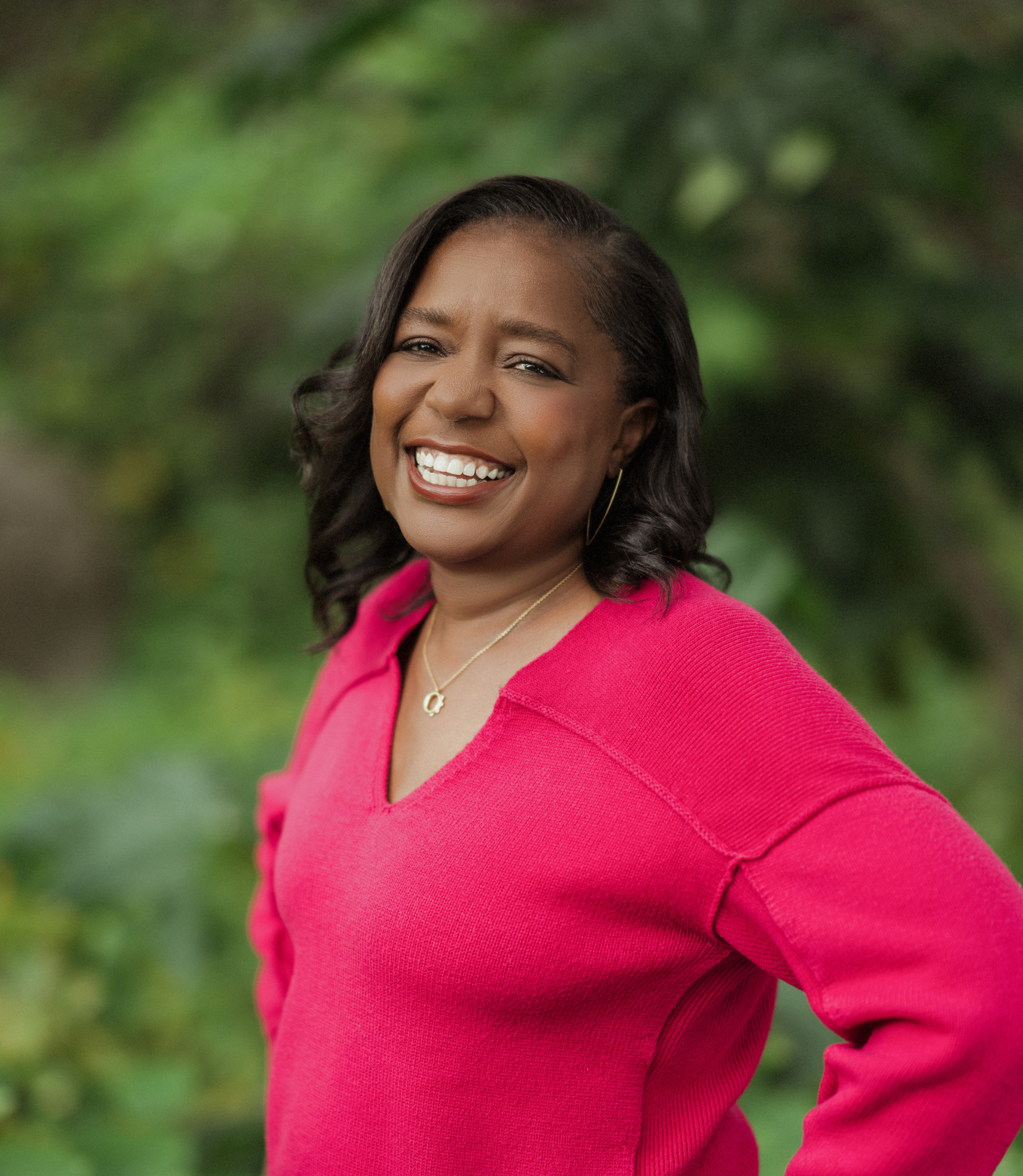 Kommah McDowell portrait in a fuchsia sweater with greenery behind her